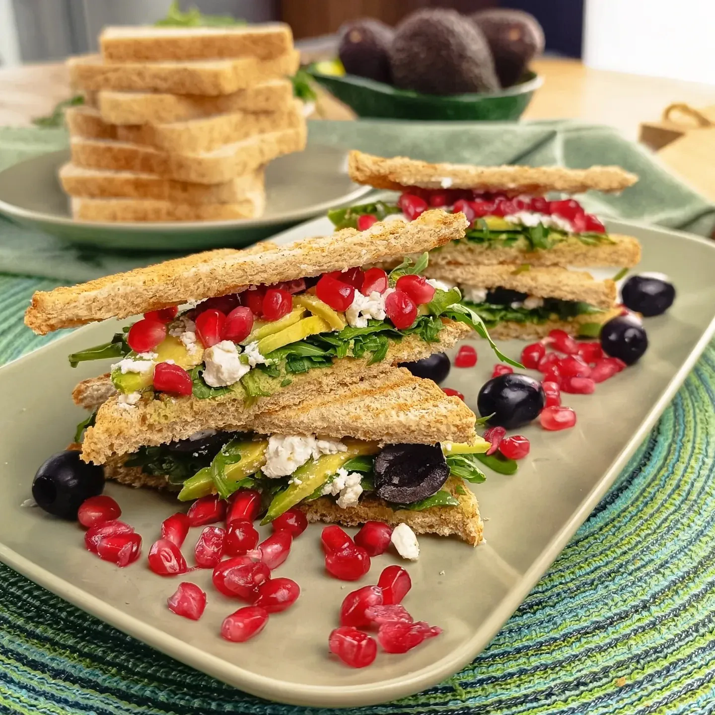 Zdrowe tosty śniadaniowe z awokado, rukolą, fetą, granatem i czarnymi oliwkami